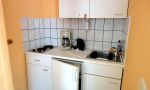 linke Hälfte vom Doppelbungalow zum Gehweg hin mit Terrasse, Bad mit Dusche und WC, Schlafzimmer mit Doppelbett und Einzelbett, Wohnzimmer mit Couch und Fernseher sowie eine kleine Pantry Küche