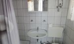 linke Hälfte vom Doppelbungalow zum Gehweg hin mit Terrasse, Bad mit Dusche und WC, Schlafzimmer mit Doppelbett und Einzelbett, Wohnzimmer mit Couch und Fernseher sowie eine kleine Pantry Küche